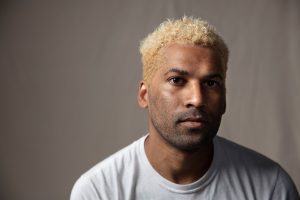 Chip Miller - a headshot of a black person with short blond hair on a neutral beige background