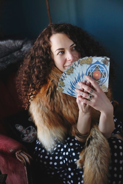 Photo of Carrie Parker a white woman with long curly hair seated holding splayed cards
